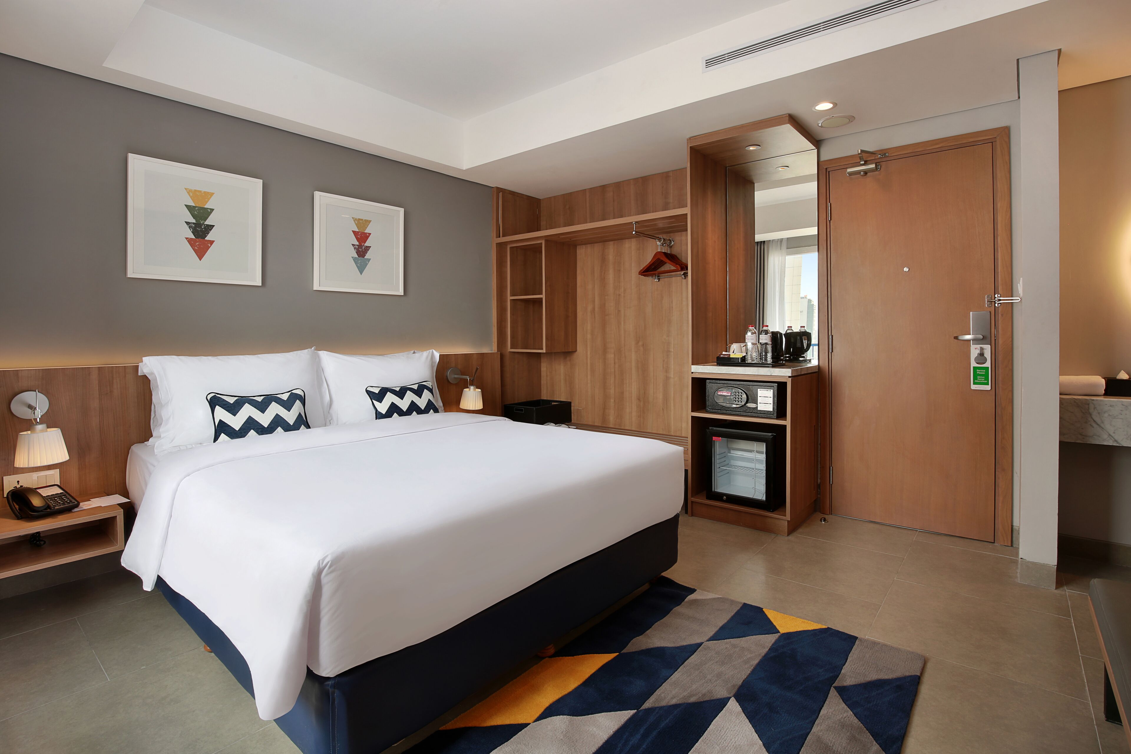 A hotel room with a large bed, a desk with a lamp, a wardrobe, and a mirror.