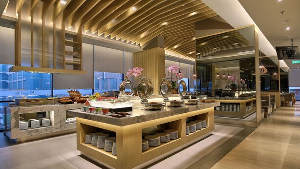 A modern hotel lobby with a marble reception desk, wooden accents, and a view of the cityscape through large windows.