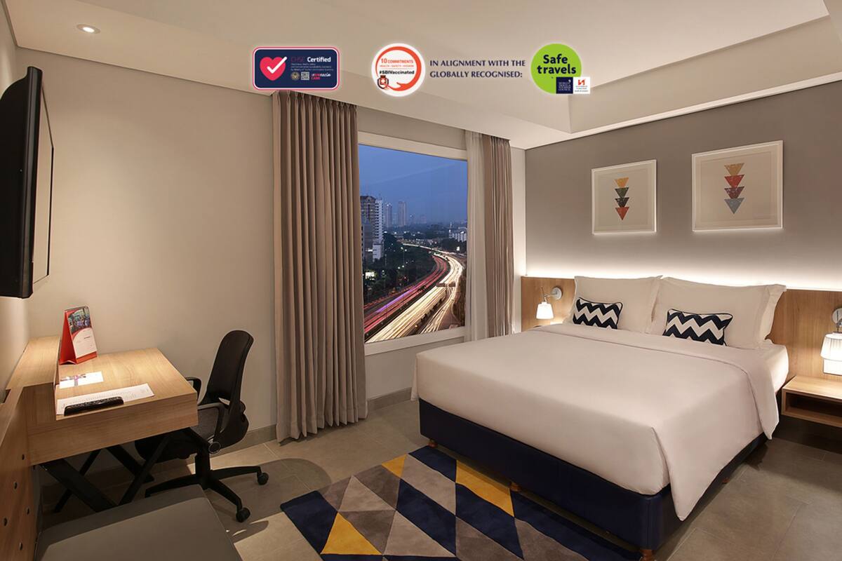 Une chambre d’hôtel avec un grand lit, un bureau avec une chaise, une télévision et une vue sur le paysage urbain.