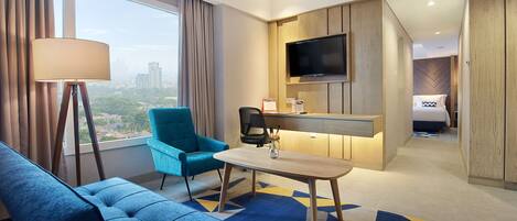 A modern hotel room with a large window, a sofa, a chair, a desk, and a bed.