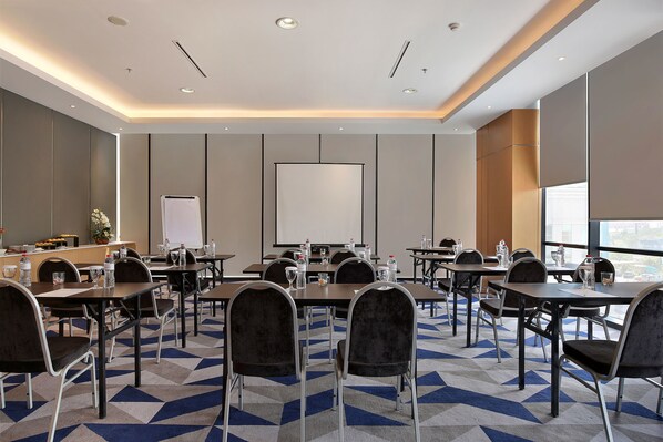 Un salón de conferencias con mesas, sillas, una pizarra y un amplio ventanal.