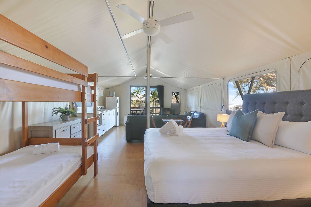 A bedroom with a bunk bed, a single bed, a ceiling fan, and a view of the outside.