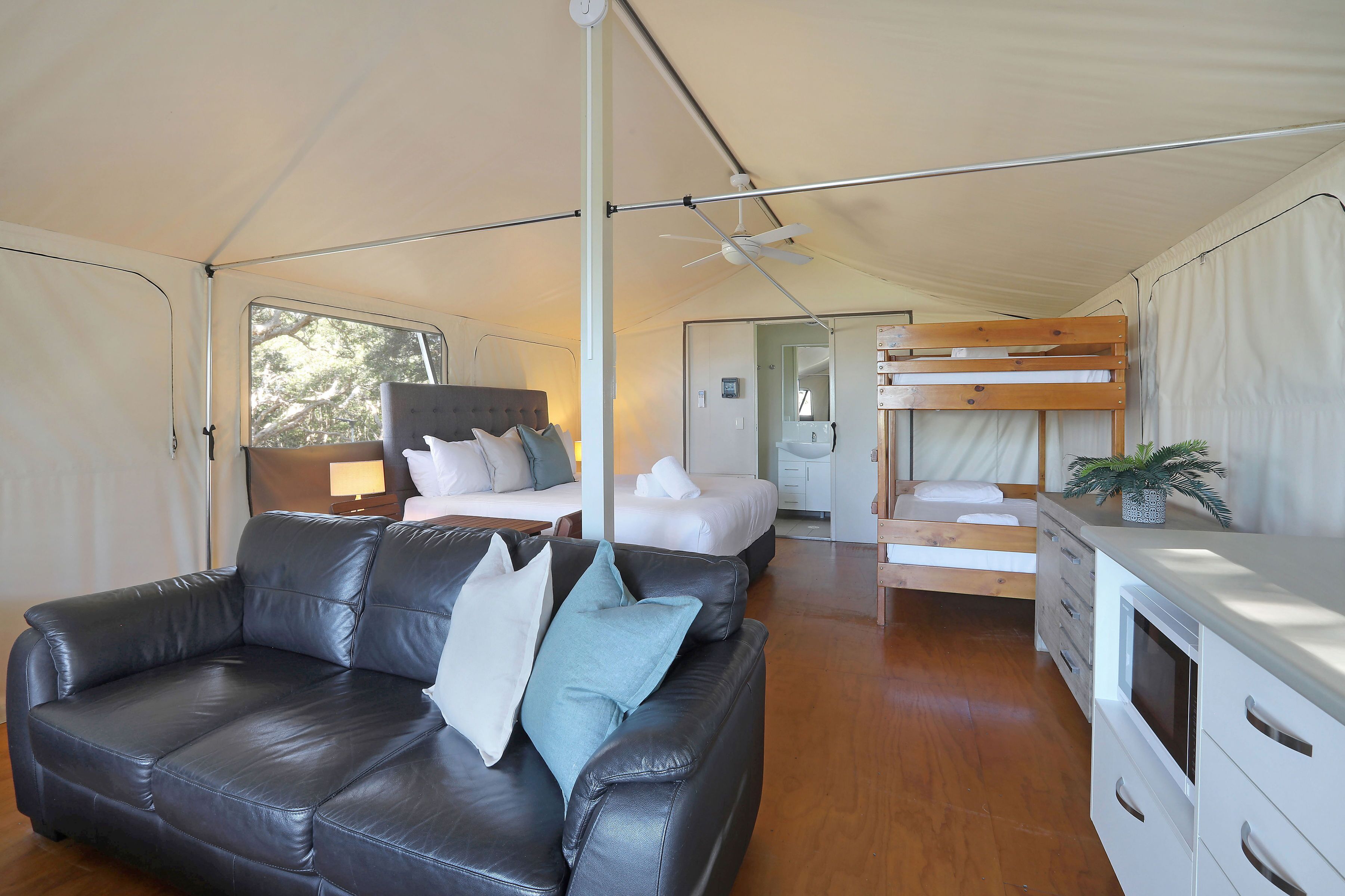 Un hébergement sous tente comprenant un canapé en cuir, un lit superposé, un coin cuisine et un plancher en bois.