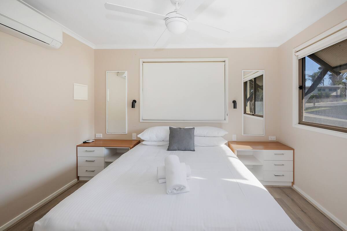 A hotel room with a bed, bedside tables, a ceiling fan, a window, and a view of the outside.