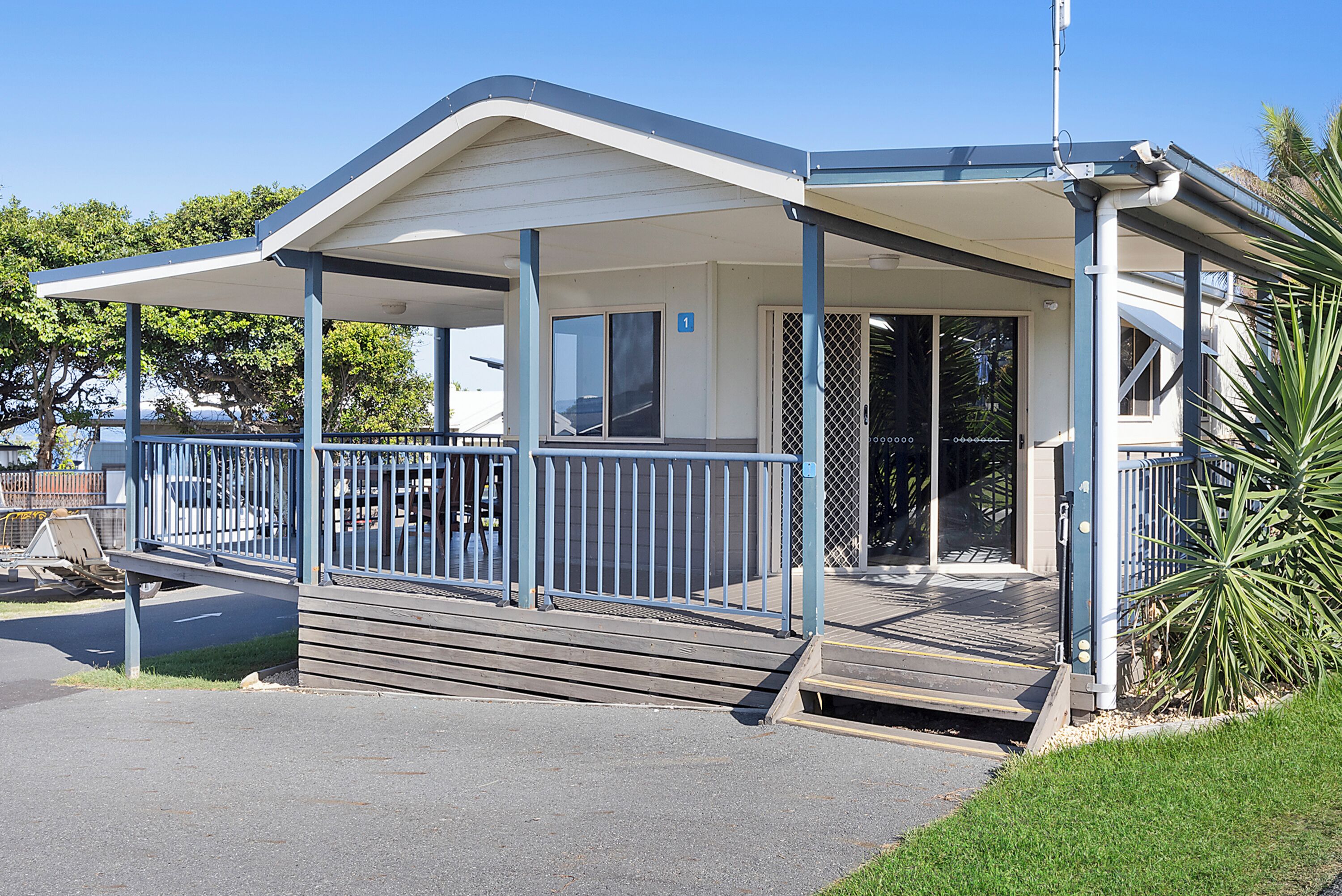 A covered outdoor area with a wooden deck, metal railing, and a door leading to a building.