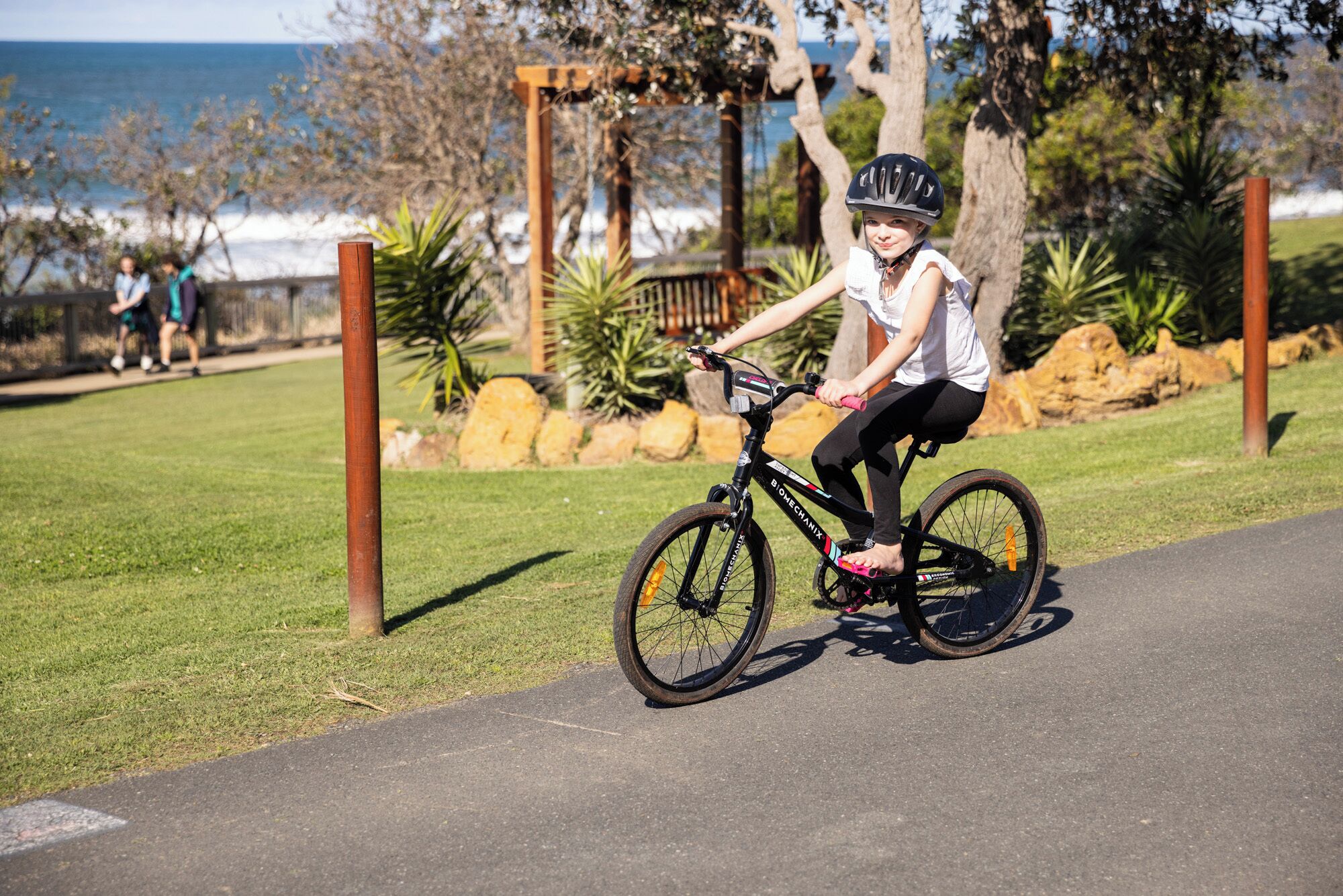 Una persona che pedala su una pista ciclabile in un parco con erba e alberi.