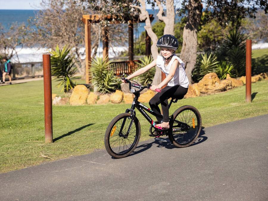 Una persona che pedala su una pista ciclabile in un parco con erba e alberi.