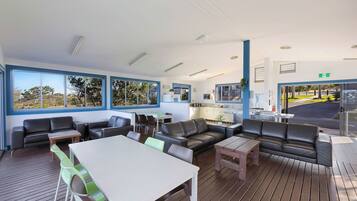 A modern lounge area with leather sofas, a dining table, and large windows offering views of the outdoors.