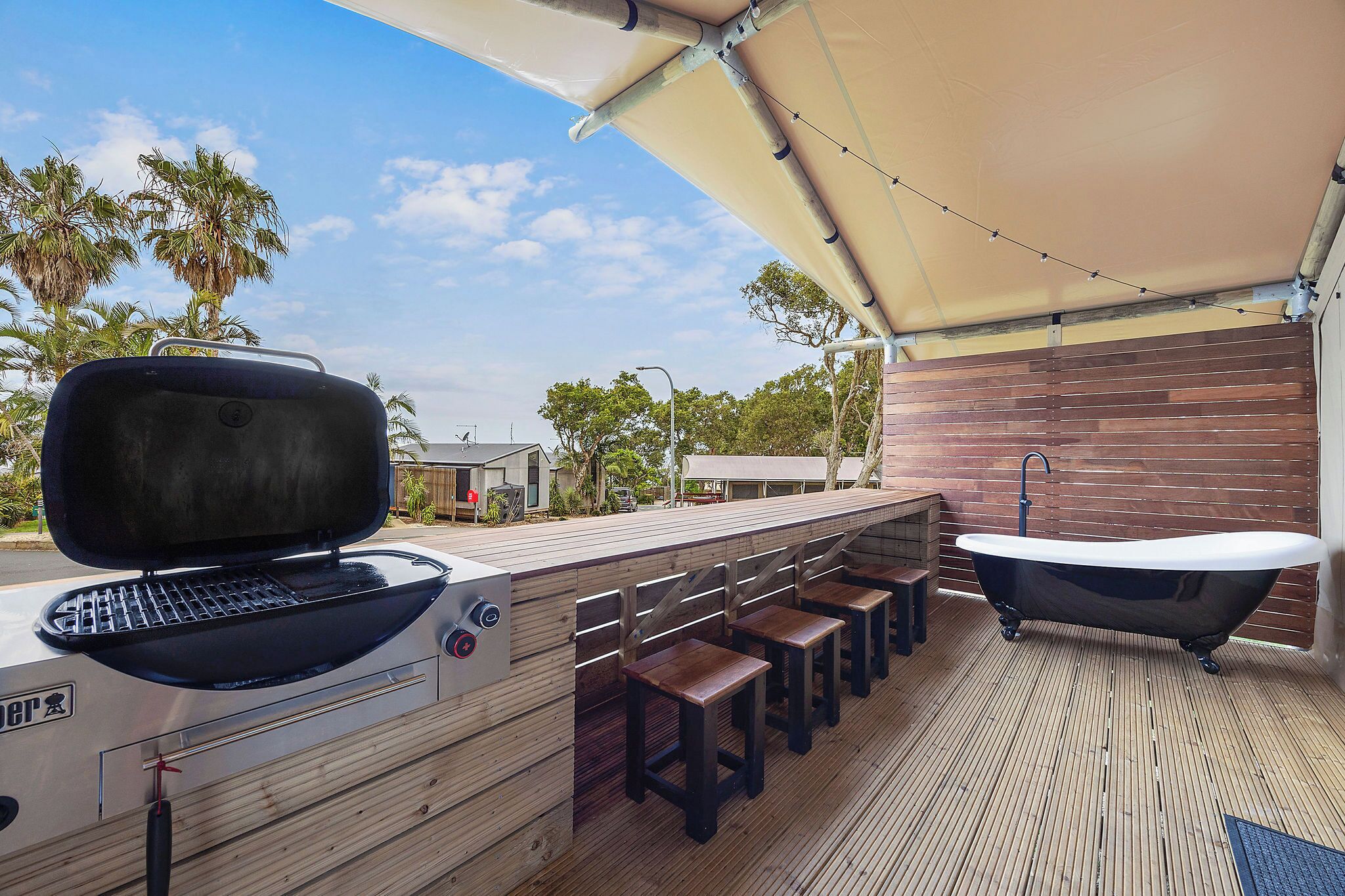 Un espace bar extérieur comprenant un barbecue, des tabourets de bar et une baignoire.