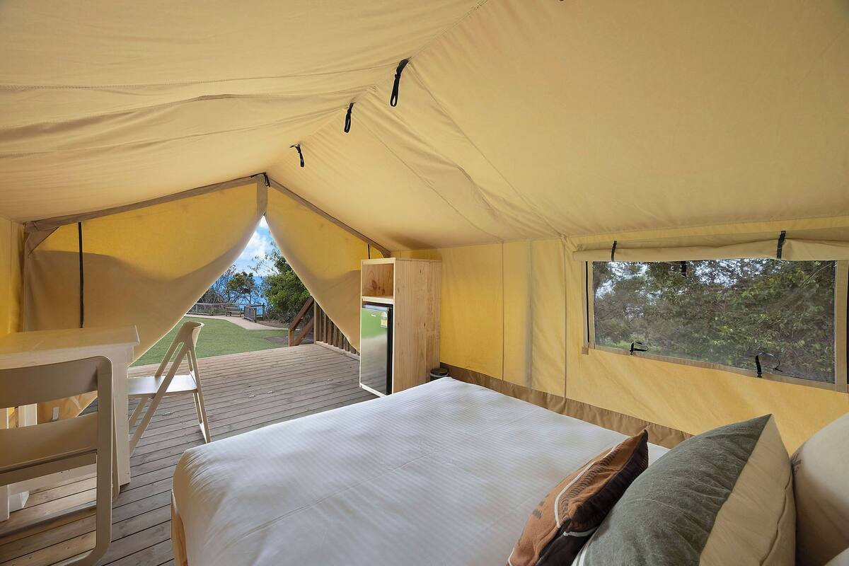 A tented accommodation with a bed, a window, and a view of the outdoors.
