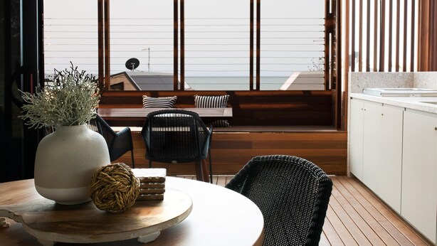 A modern kitchen with a large window, a round dining table, and a black wicker chair. - Reflections Bonny Hills - Holiday Park (Bonny Hills)
