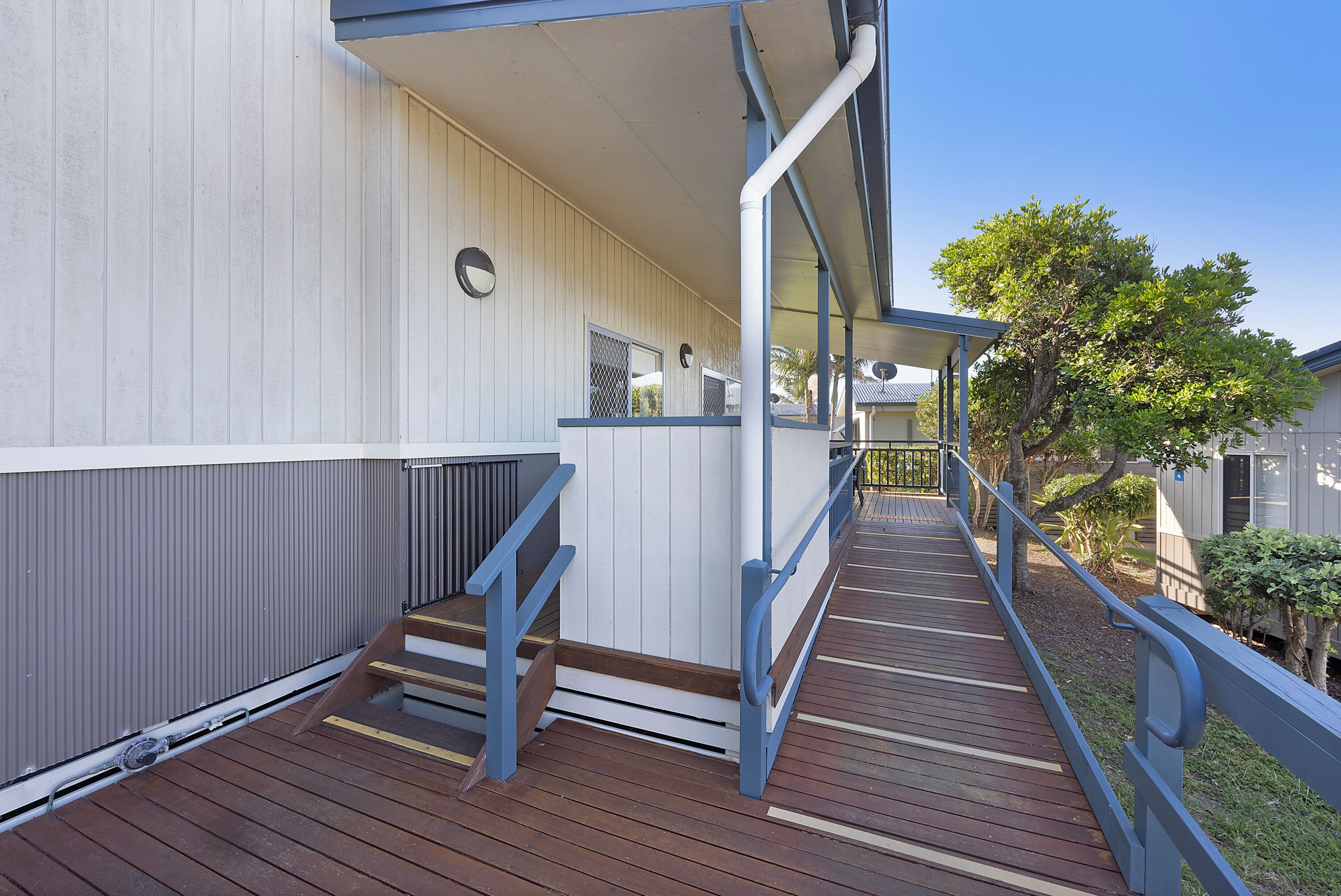 A wooden deck with a metal railing leading to a building with a white exterior and a blue roof.