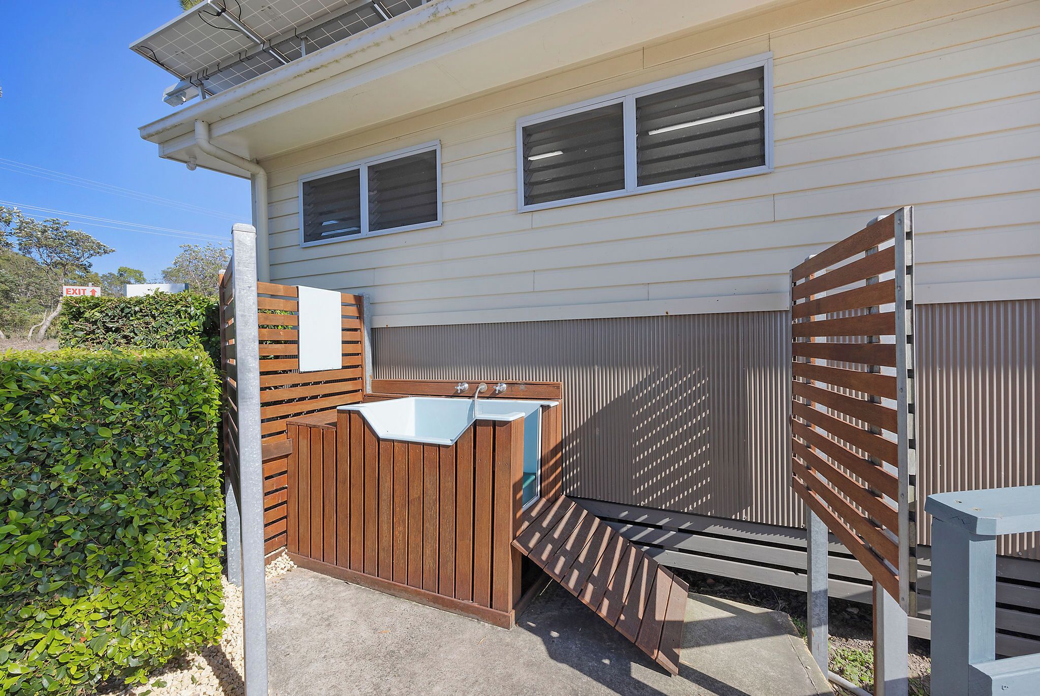 A modern outdoor bathroom with a wooden enclosure, a sink, and a bench.