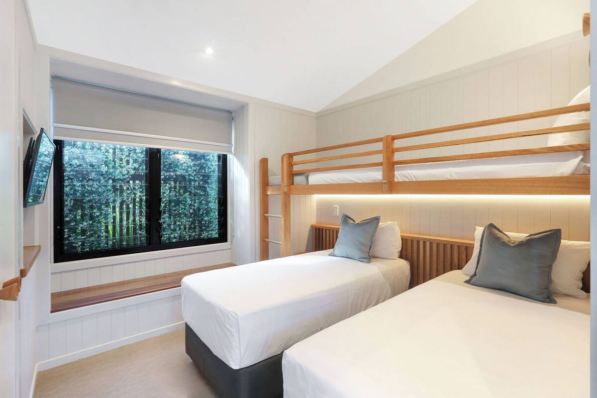 A bedroom with two beds, a large window with a view of trees, and a built-in TV.
