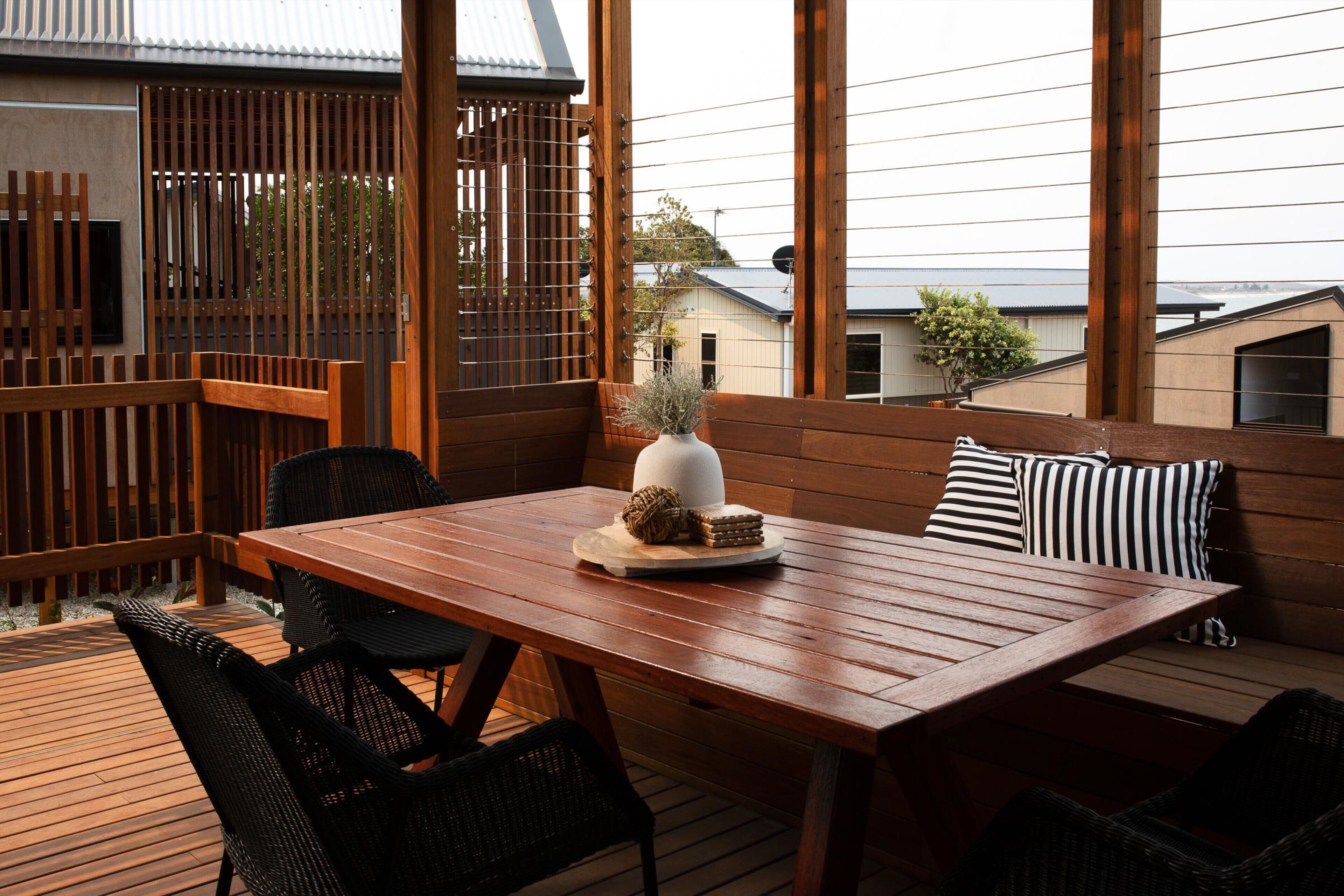 Una terraza de madera con una mesa, sillas, un florero decorativo y un cojín a rayas.