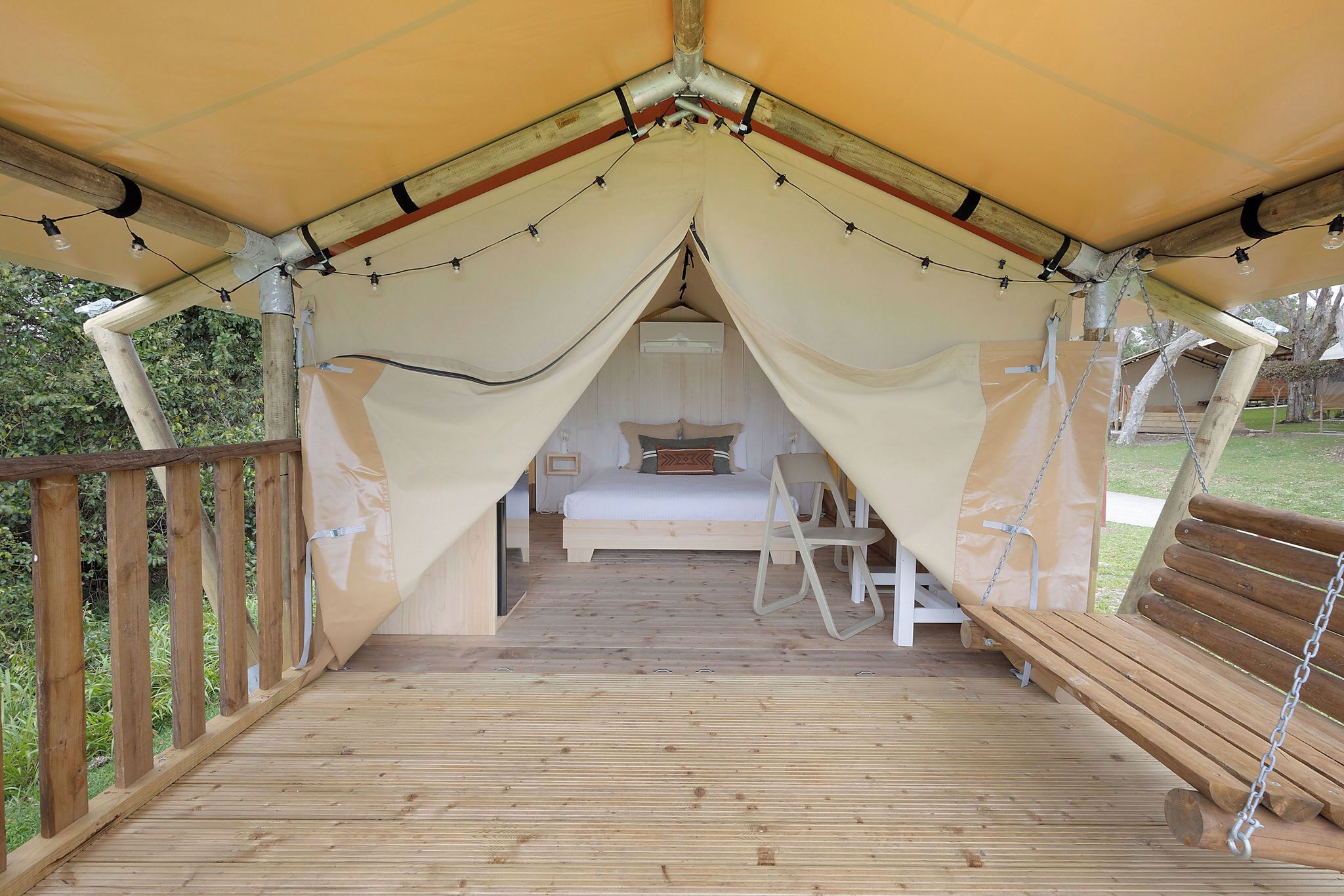 Eine Zelthütte mit Holzterrasse, einem Bett und einem Schaukelstuhl.