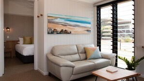 A modern living room with a beige leather sofa, a wooden coffee table, and a painting of a beach scene. - Reflections Bonny Hills - Holiday Park (Bonny Hills)