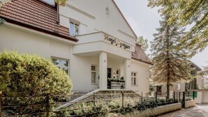 Un bâtiment à deux étages, sur lequel on peut lire l’inscription « Hôtel Grottinger ». Il est doté d’un escalier en pierre menant à une entrée couverte, qui est entourée de verdure et d’une clôture en métal.