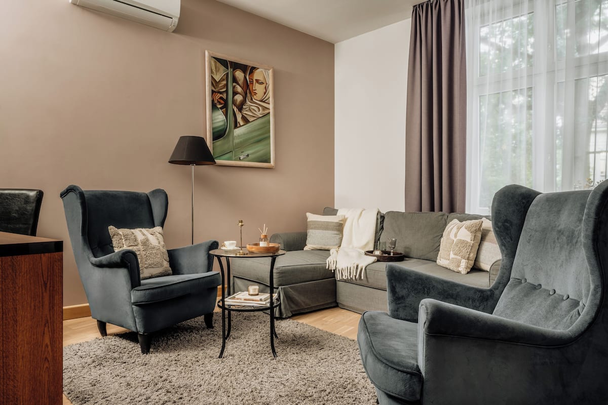 A modern living room with a grey sofa, two armchairs, a small side table, and a painting on the wall.