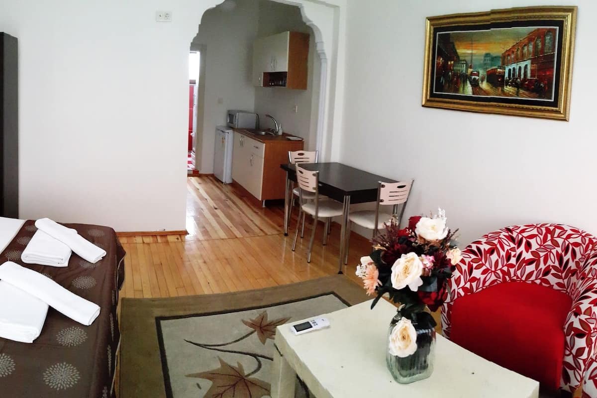 A hotel room with a bed, a small table with a vase of flowers, a red chair, and a painting on the wall.