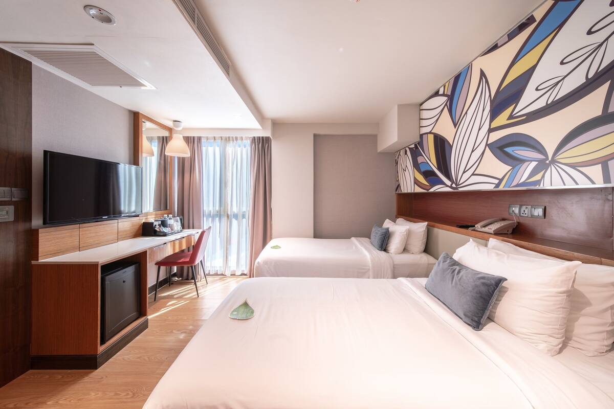 A hotel room with a flat-screen TV, a desk, two beds, a mirror, and a large floral wall mural.