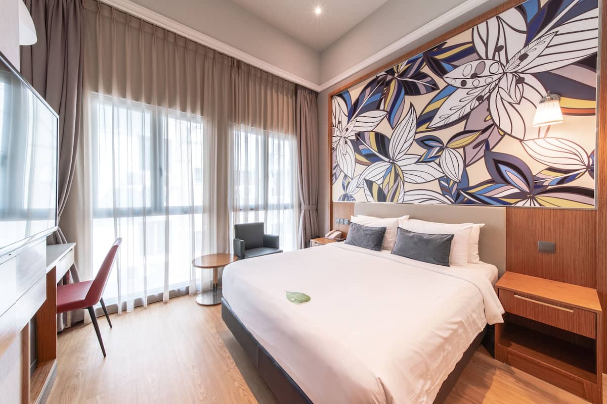 A hotel room with a large bed, a desk, a chair, and a wall with a floral mural.