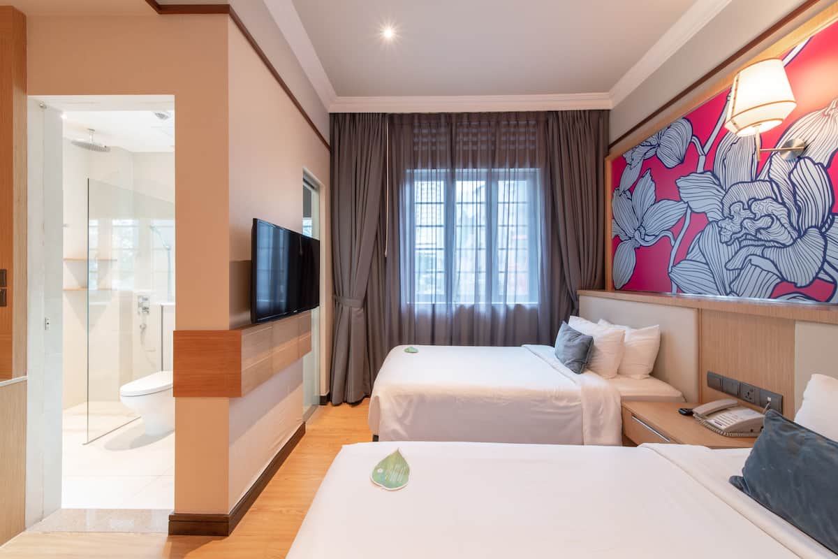 A hotel room with two beds, a TV, a bathroom, and a large floral artwork on the wall.