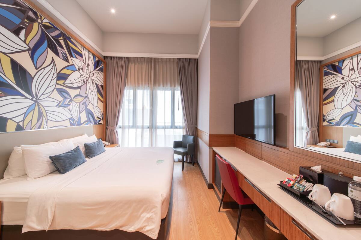 A hotel room with a bed, a desk, a television, and a large mirror.