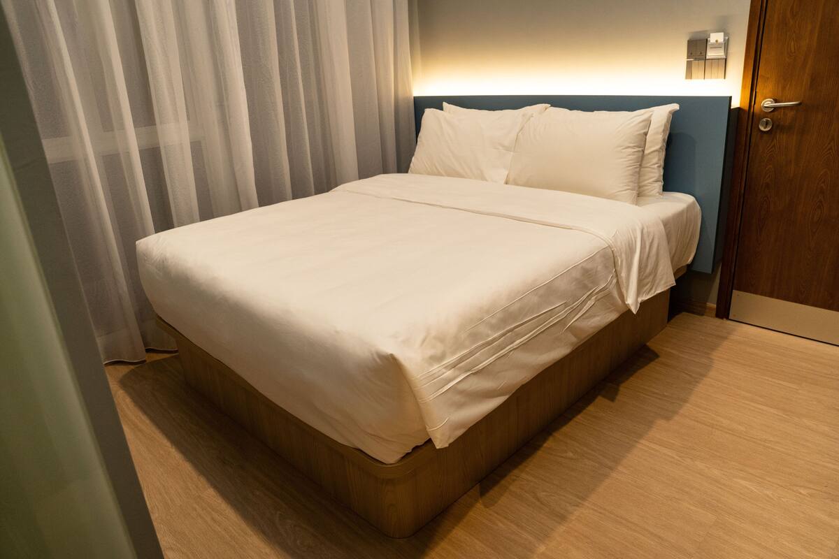 A neatly made bed with a wooden headboard and a light-colored bedspread.