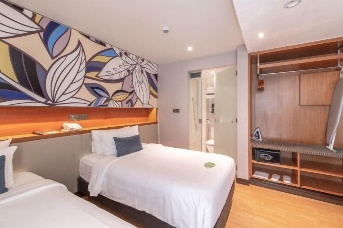 Habitación de hotel con dos camas individuales, cabecero de madera, un amplio mural floral en la pared y un armario empotrado con estantes.