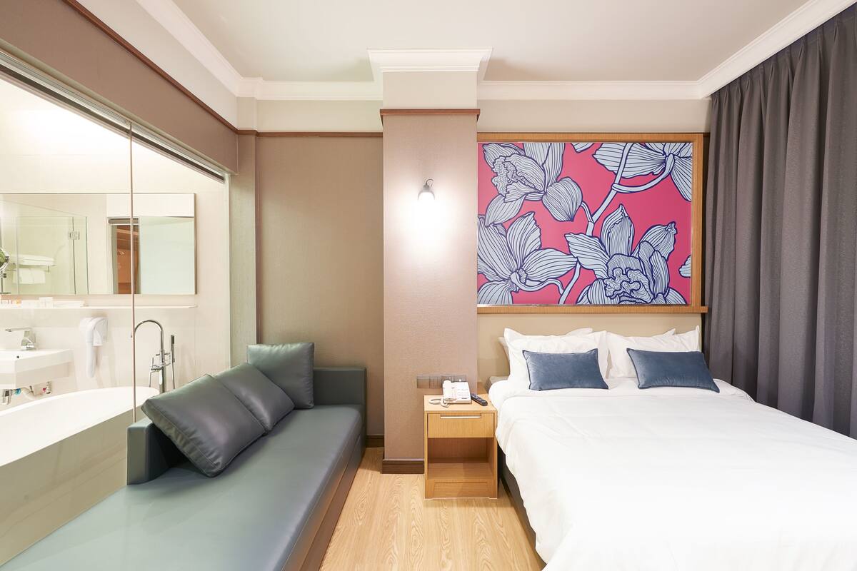 A hotel room with a bed, a sofa, a nightstand, a mirror, and a bathroom.