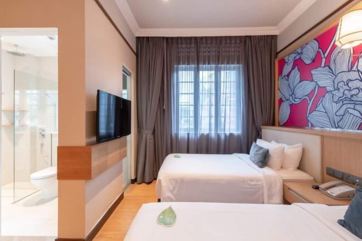 A hotel room with two beds, a TV mounted on the wall, a large window with curtains, and a floral artwork on the wall.
