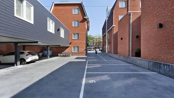 Een parkeerplaats met aangegeven parkeerplaatsen, een witte auto en een gebouw met bakstenen muren en ramen.
