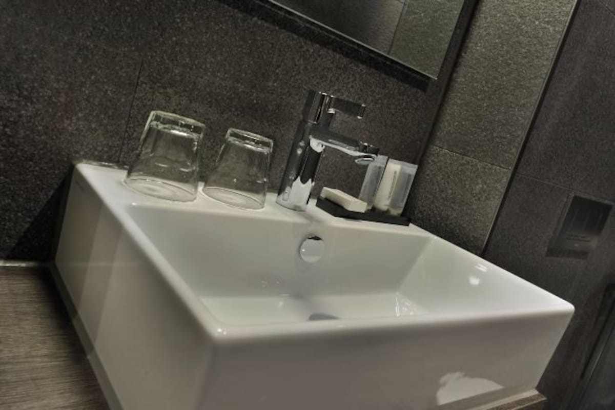 Un baño moderno con un lavabo blanco, dos vasos de vidrio y un grifo de cromo.