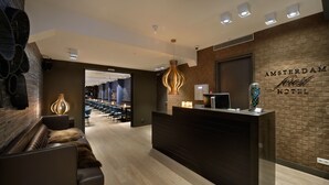 Un área de recepción moderna de hotel con un mostrador oscuro, un sofá de cuero y una pared de ladrillo decorativa.