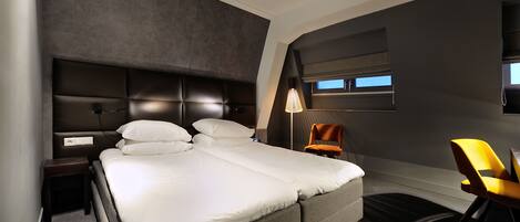 A modern hotel room with a large bed, a nightstand, a desk, and a chair.