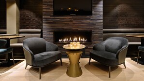 Un área de estar moderna con chimenea, dos sillones, una mesa redonda y un televisor montado en la pared.