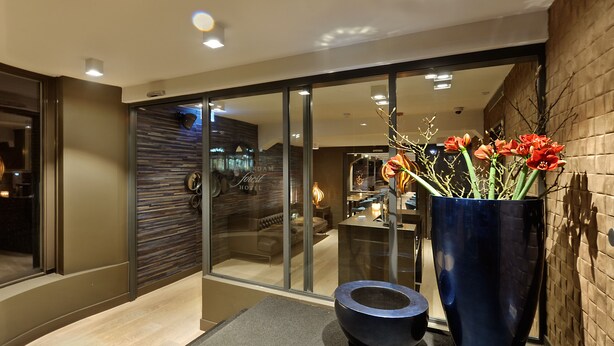 Un moderno vestíbulo de hotel con un panel de vidrio, un jarrón azul grande con flores rojas y un tazón negro sobre una encimera gris.