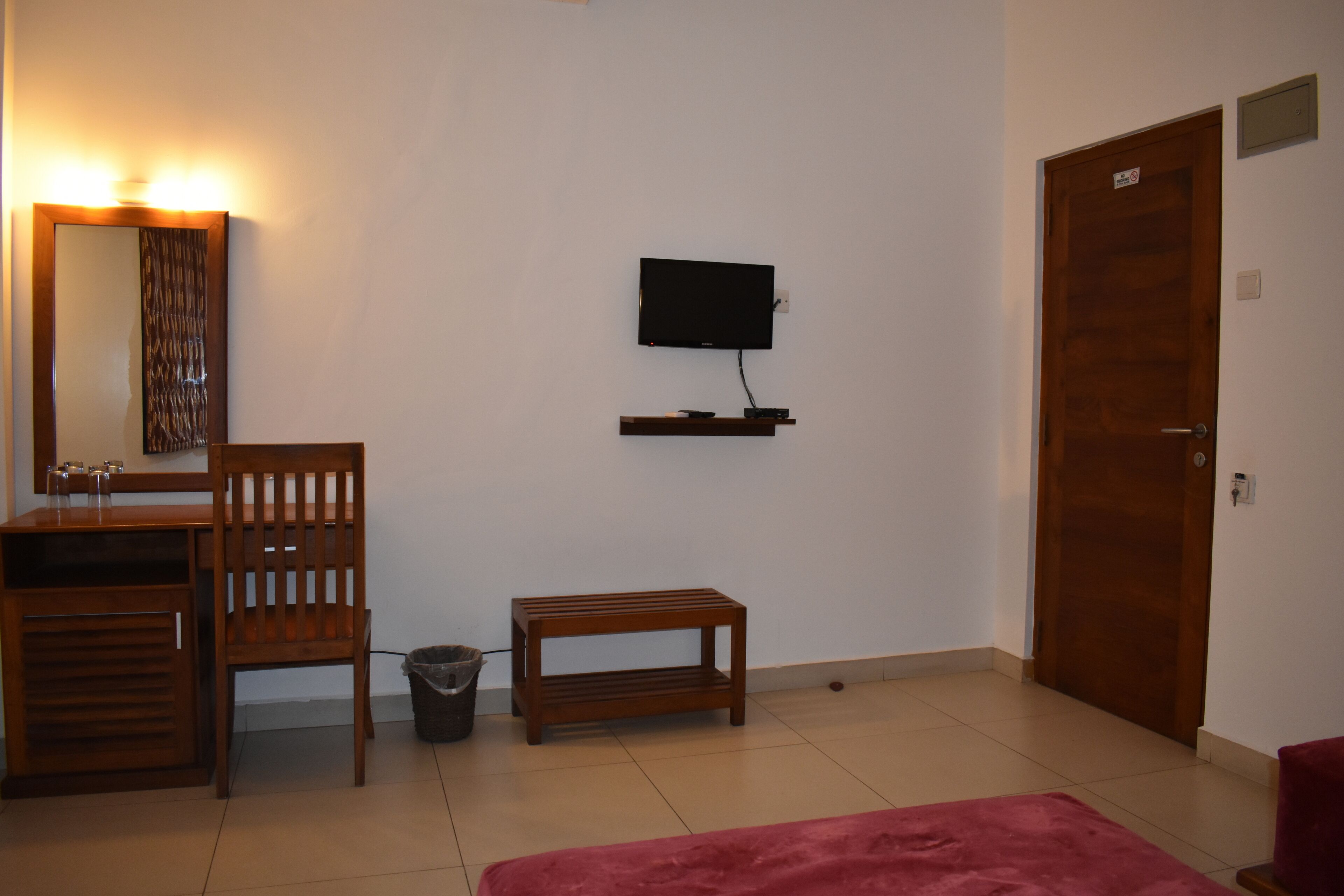 Una habitación con un escritorio de madera, una silla, un televisor en la pared, una pequeña mesa de madera y una puerta.