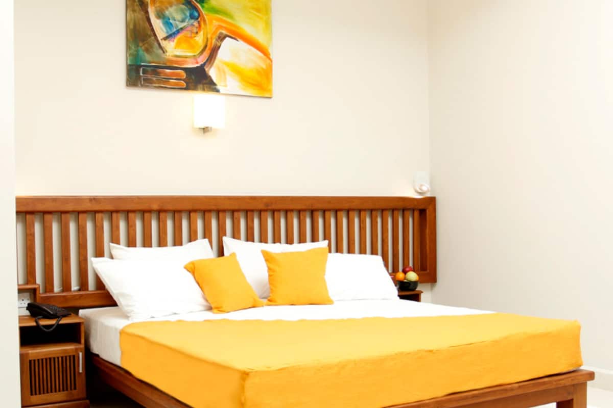 A neatly made bed with a wooden headboard, white and yellow pillows, and a yellow bedspread.