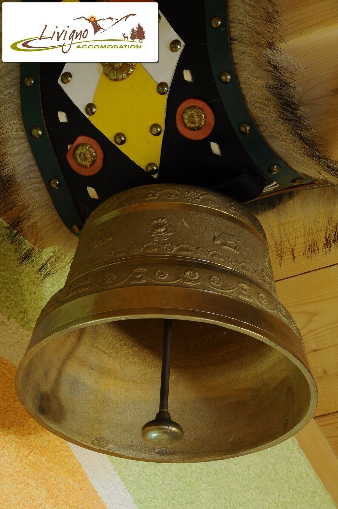 A brass bell with intricate designs, mounted on a decorative metal structure with a fur-like texture.