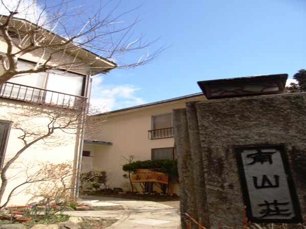 A building with a stone sign, a tree, and a clear sky. - Nanzansou (Ome)