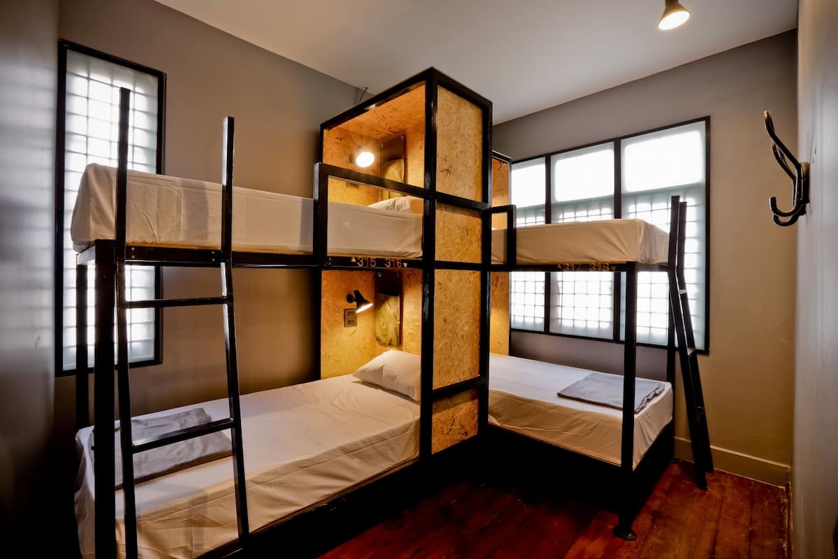 A bunk bed room with wooden frames, a small window, and a wall-mounted light.
