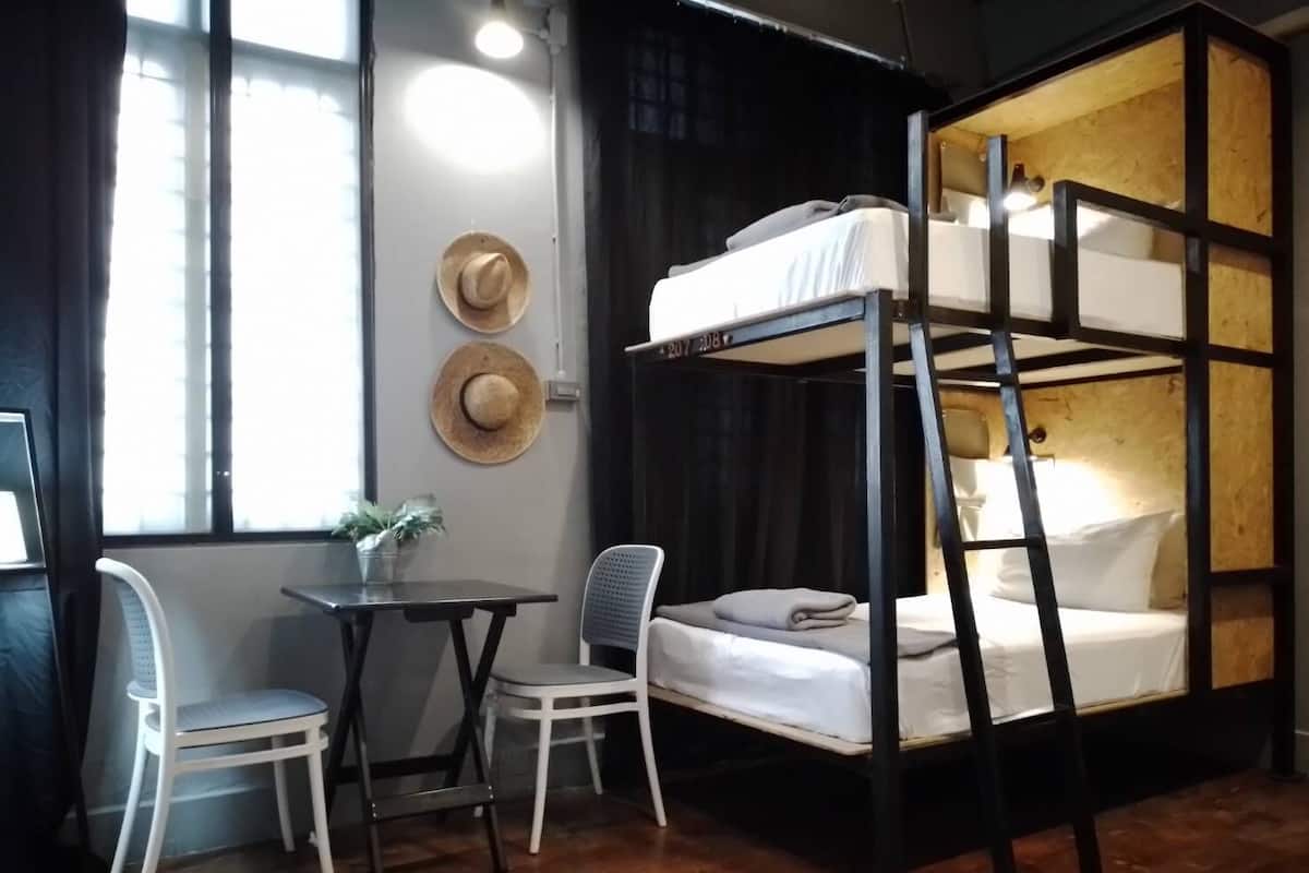 A bunk bed with a desk and two chairs in a room with a window and hats on the wall.