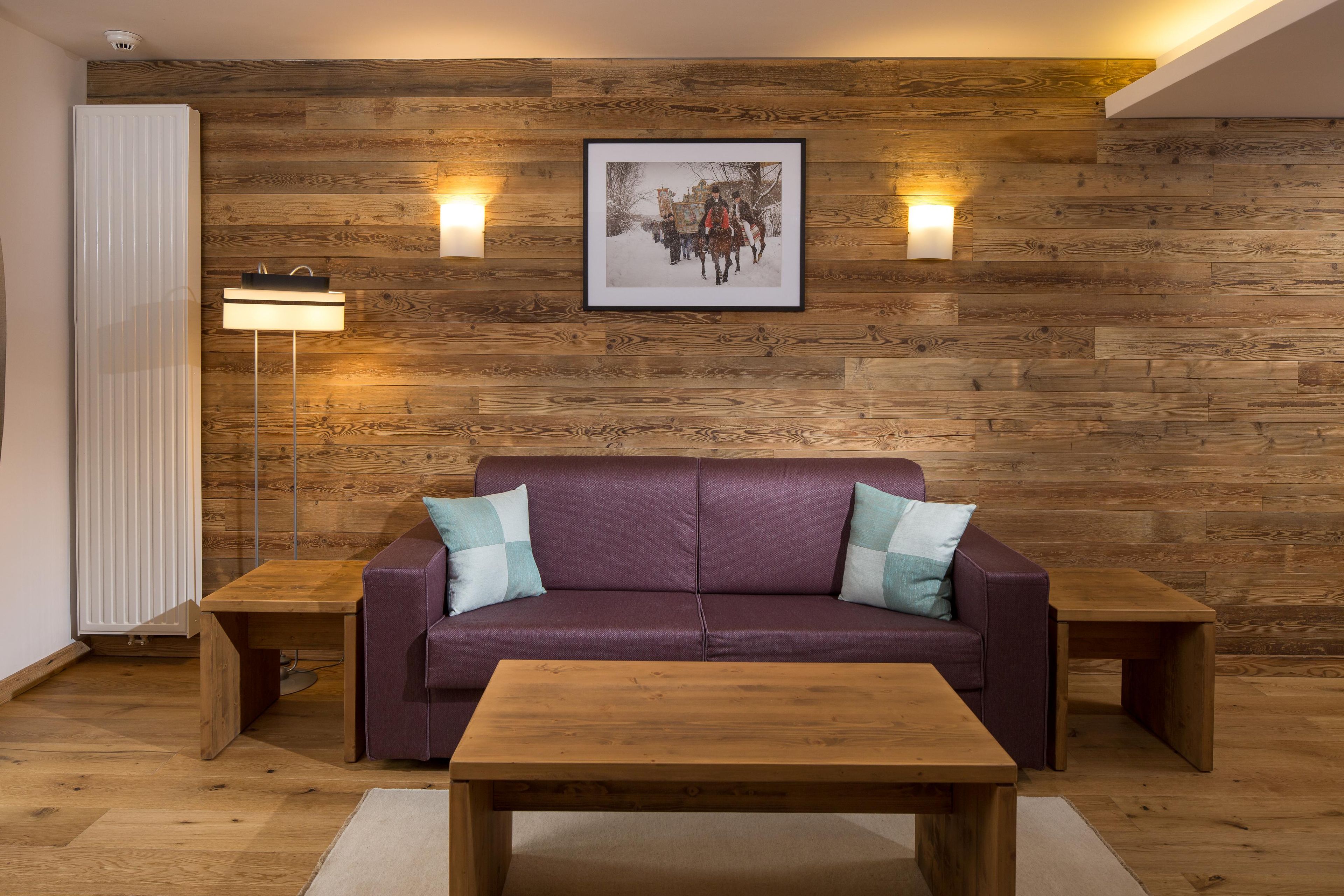 A room with a wooden wall, a purple sofa, two side tables, a framed picture, and a floor lamp.
