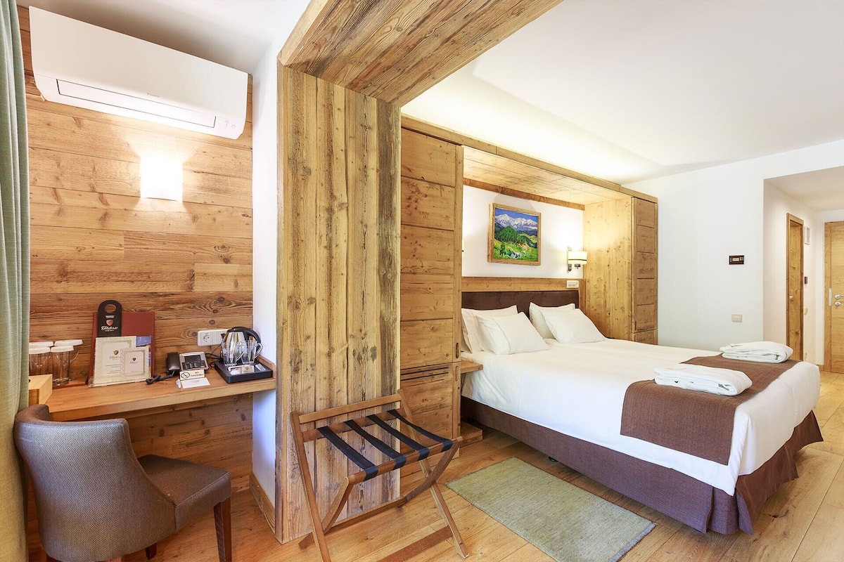 A hotel room with a wooden wall, a bed with white linens, a desk with a chair, and a painting on the wall.