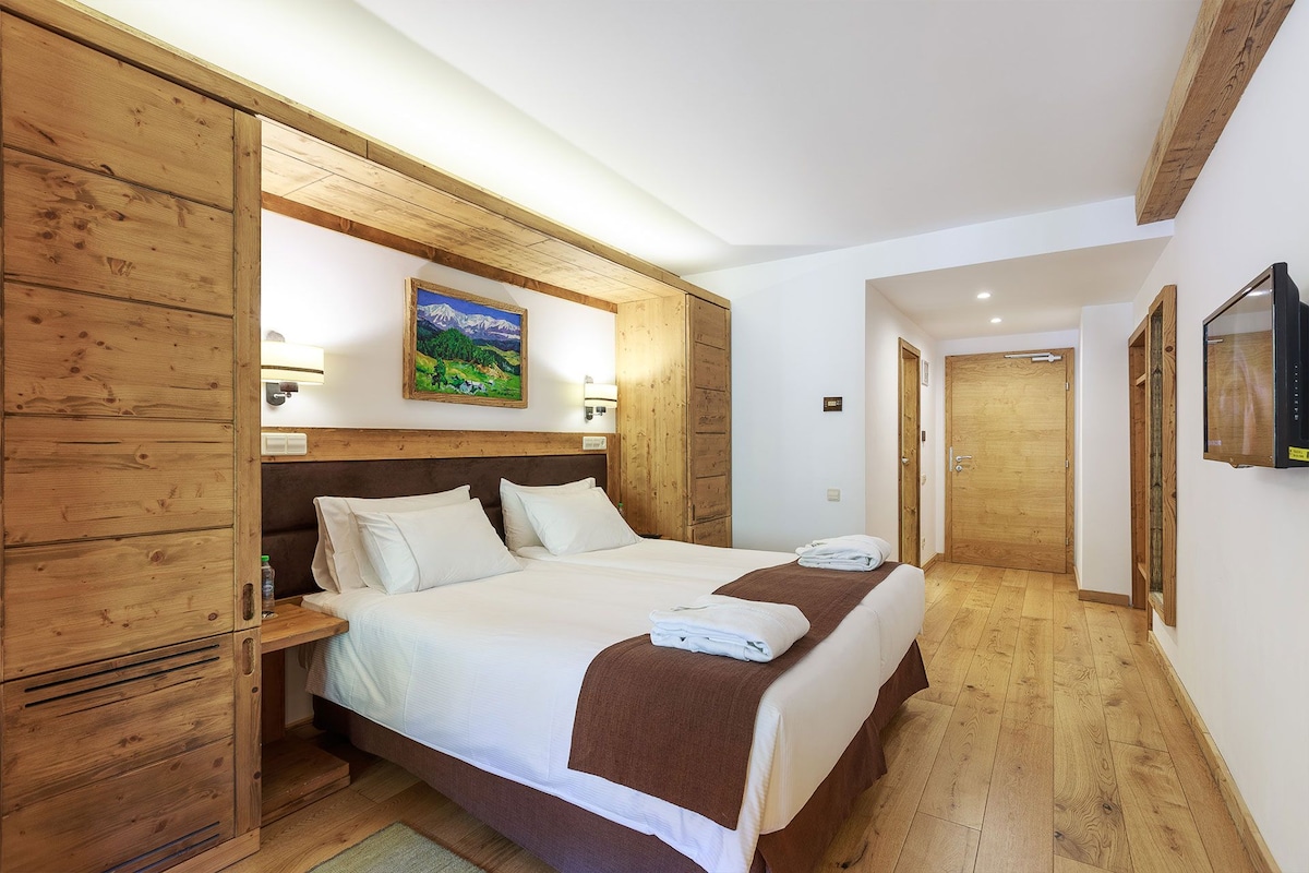 A hotel room with a wooden headboard, two beds, a painting, and a wooden wardrobe.