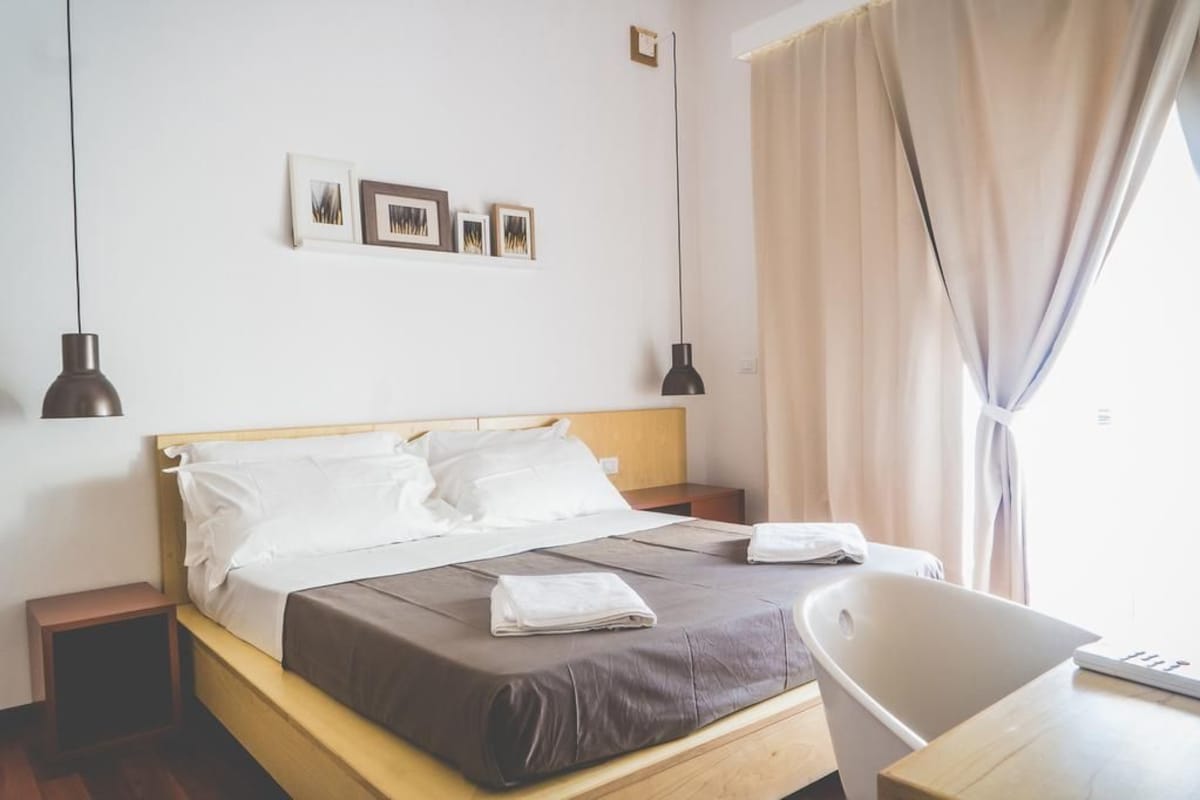 Una habitació d'hotel amb un llit, taules de nit, una cadira i un escriptori.