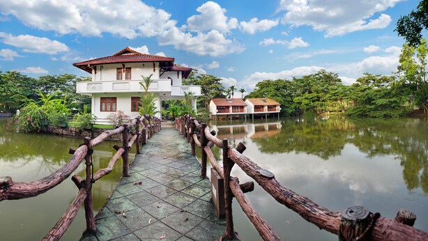 A wooden bridge leading to a two-story house with a tiled roof, surrounded by water and greenery. - Wet Water Resort (Gampaha)