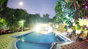 A swimming pool with a surrounding deck, lounge chairs, and a building in the background. - Wet Water Resort (Gampaha)